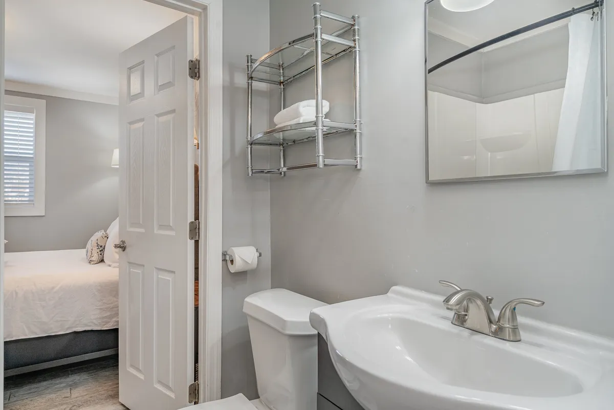 A bathroom with a clean sink, mirror, and towels on a rack, with a doorway leading directly to a bedroom. The layout visually implies a Jack-and-Jill setup, emphasizing accessibility and privacy. The decor is calm and organized, adding to a sense of tranquility.