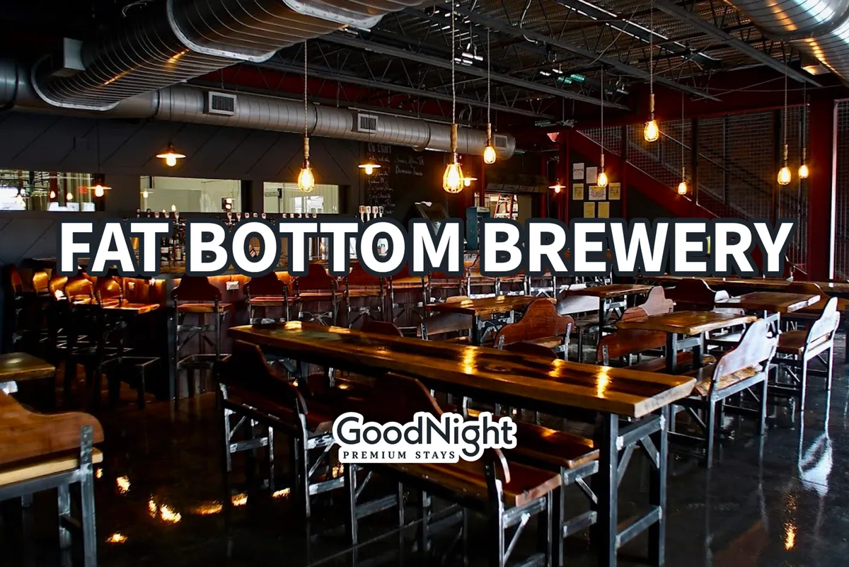 Inside a bustling brewery, this image showcases a long communal table, illuminated by warm Edison bulbs, with guests socializing over craft beers. The industrial-chic decor and visible bar area highlight the atmosphere of a local brewery or taproom, ideal for gatherings and tasting sessions.